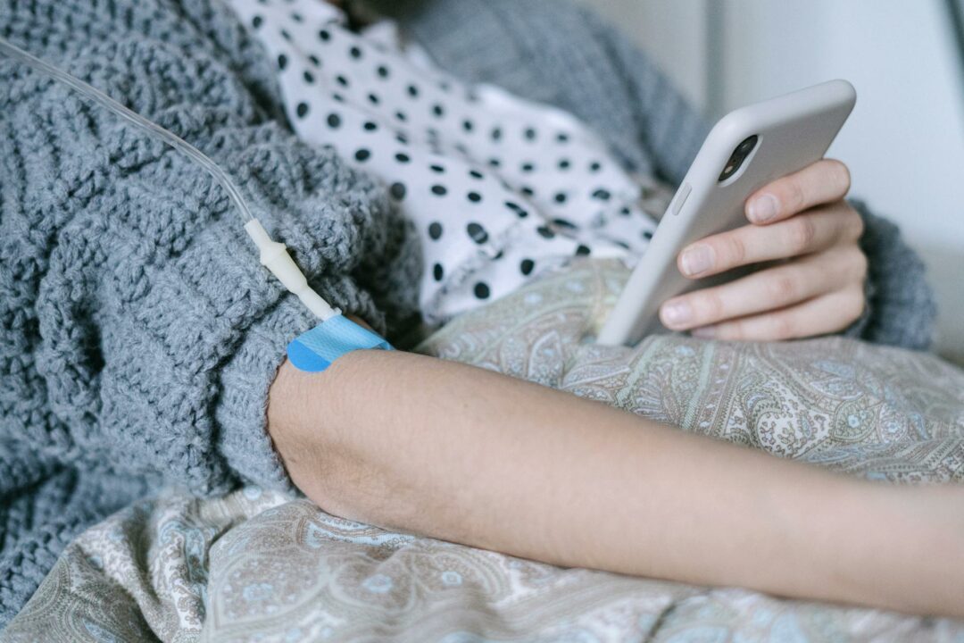 A woman receiving intravenous therapy for cancer treatment while using her phone, symbolizing connection and hope.