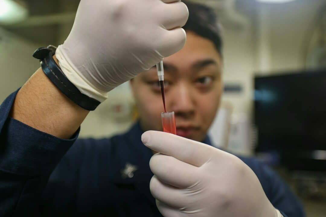 A person in gloves carefully transfers liquid into a vial